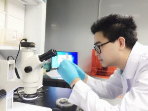 PhD Candidate Dongfang Ouyang looking at a microscope