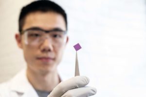 Man holds small purple square of graphene with tweezers